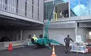 Maeda MC305C spider crane operating near a building entrance with outriggers deployed