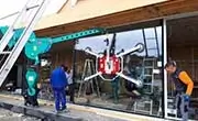Maeda MC815C mini spider crane lifting and positioning a large glass panel with workers assisting